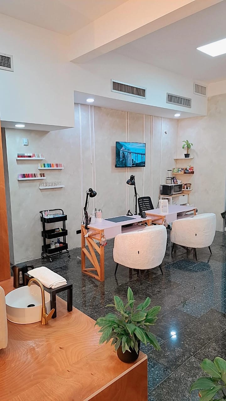 Zona de manicure de Nails Home con mesas, sillas blancas y estantería de esmaltes